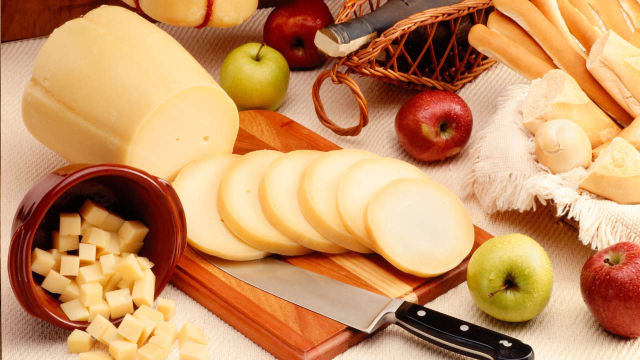 tipos diversos de queijo, incluindo o queijo defumado com maças, uma tábua de madeira e uma faca com cabo preto